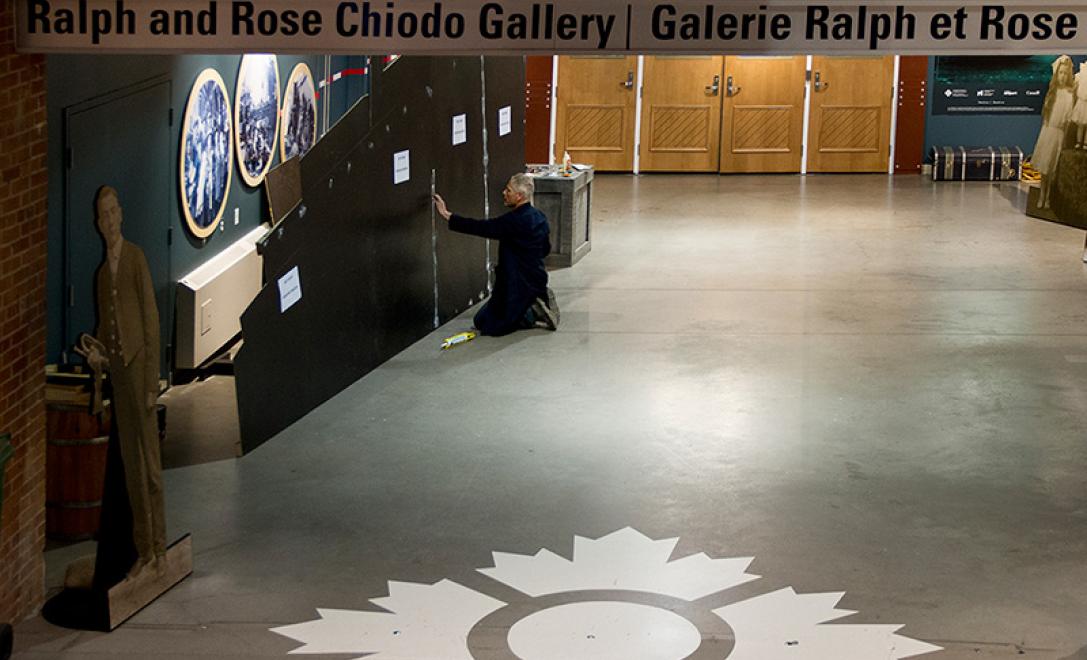 A man kneels in front of a blank canvas in the shape of a ship.