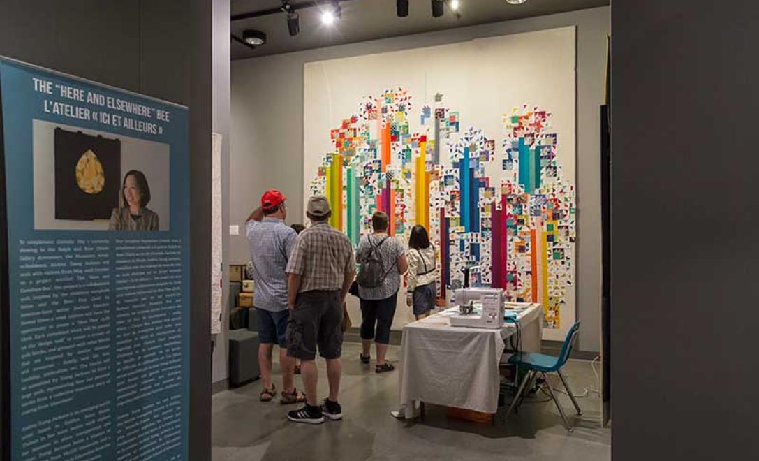 People stand in front of an incomplete quilt on the wall.