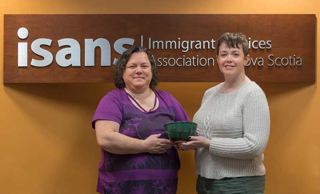 Two women stand holding a ceramic bowl between them.