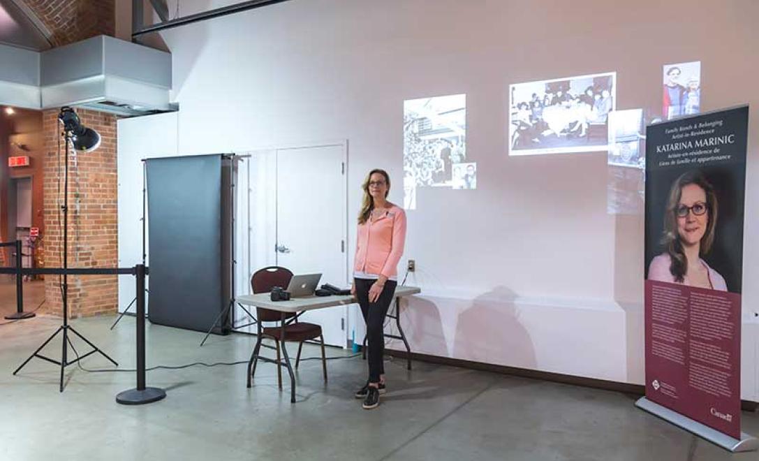 Woman in pink sweater stands next to a desk and images are projected onto the wall behind her.