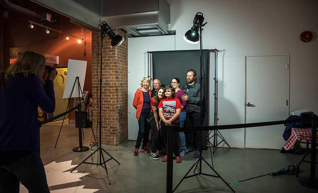 A family stand in front of a black backdrop and pose for a photo.