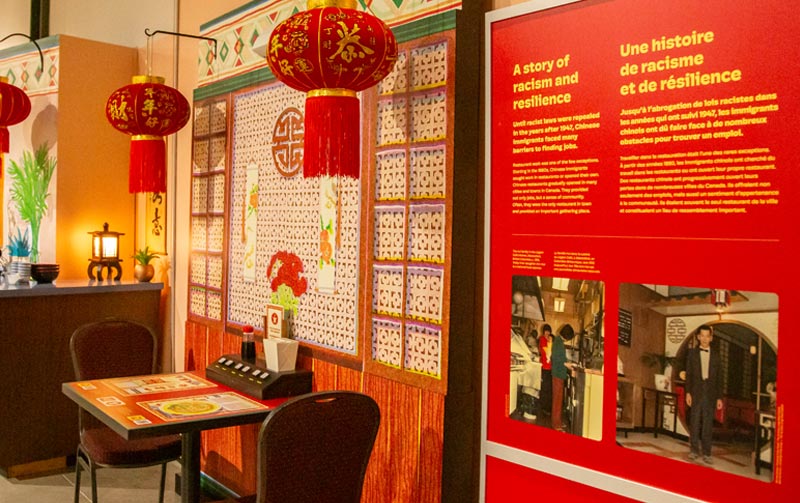 An exhibit that looks like a Chinese Canadian restaurant with a small dining table, two chairs and red lanterns.