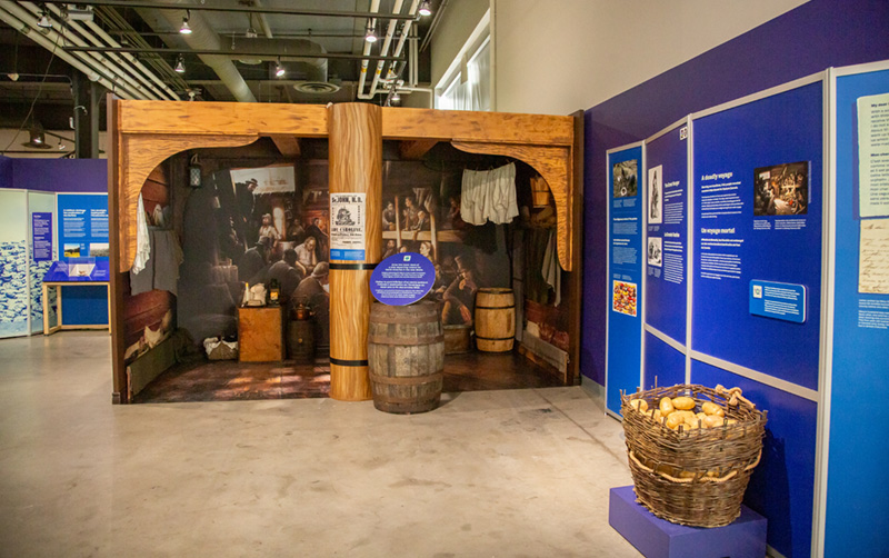 A model room showing the inside of an old ship, with several props and a large picture of people in bunks.