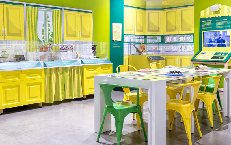 An exhibit designed to look like a kitchen with a dining table, chairs and display cases.