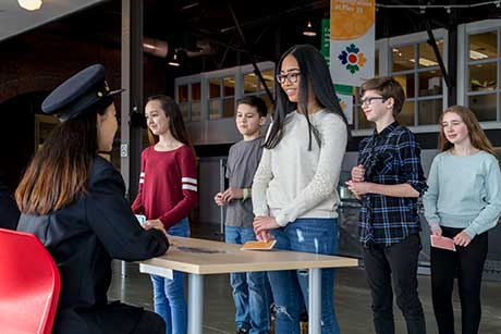 A group of children stand in front of a heritage interpreter dressed as an immigration officer.