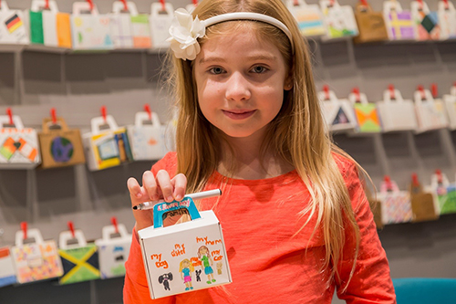 A little girl holds up a paper suitcase she has decorated.