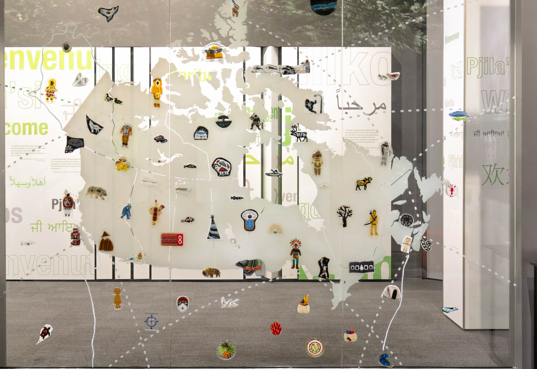 A wall-sized glass map of Canada is adorned with over seventy miniature artworks of various colours, shapes, and sizes.