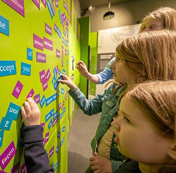 Young girls create sentences on the wall with strips of magnetic-backed words.