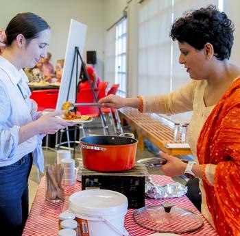 An Indian woman in a sari serves a curry to a young woman of European descent at Museum event.