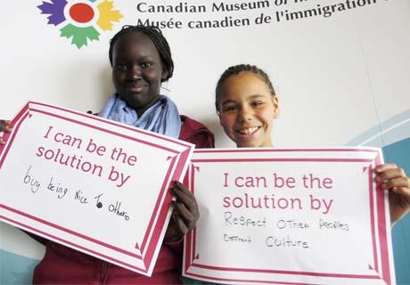 Two pre-teen students hold up signs declaring they can be nice to make the world a better place.