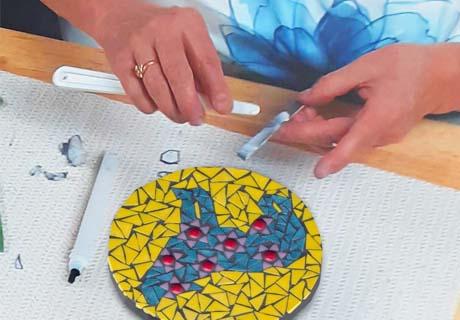 A mosaic of a blue bear with a yellow background made of glass pieces glued to the round plate.