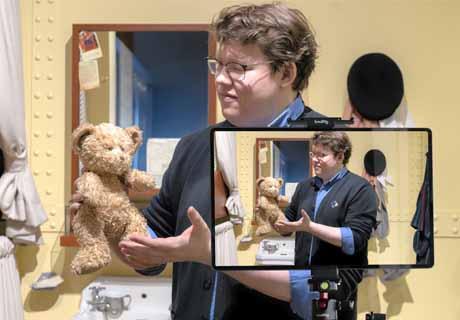 An interpretor holds up a yellow stuff bear while streaming to a classroom.