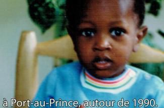 A cute little boy in a turquoise sweater sits in a chair.
