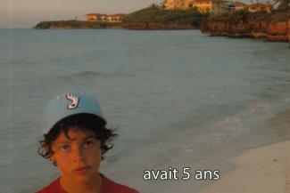 A young boy wearing a blue cap stands on a beach.
