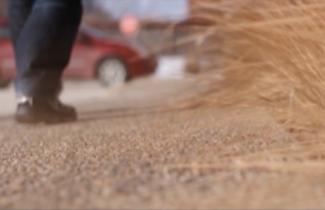 A man's shoes can be seen as the man walks on a dirt road.