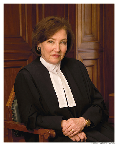 A portrait of Rosalie Silberman Abella wearing a black judicial robe with white collar tabs, seated in a wooden chair.