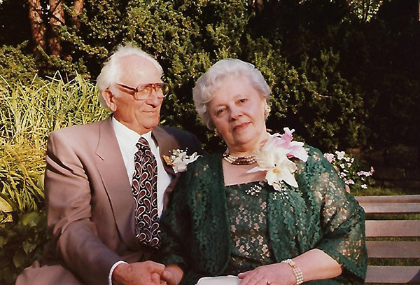 A well-dressed young couple are sitting on a bench in front of trees.