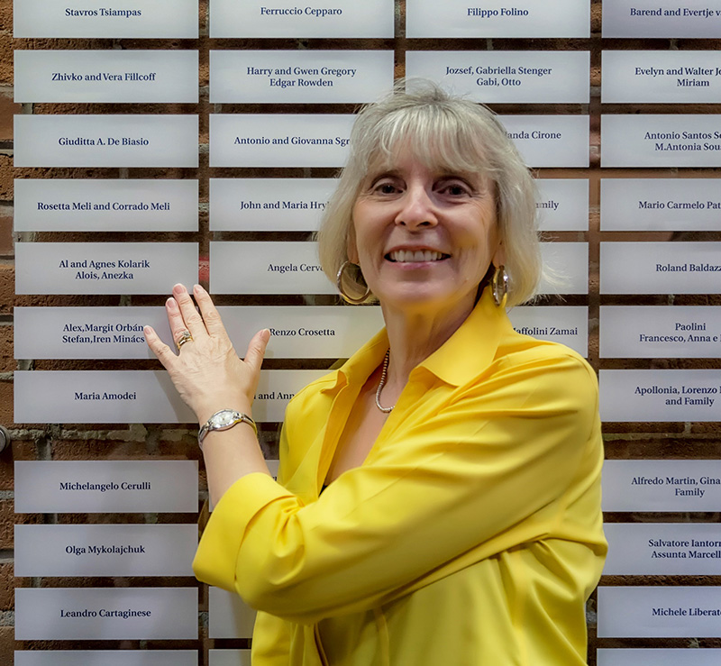 A woman wears a yellow top and is pointingat a plaque on the Sobey Wall of Honour.