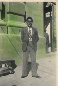 Young man wearing suit and tie standing on side walk in front of building.