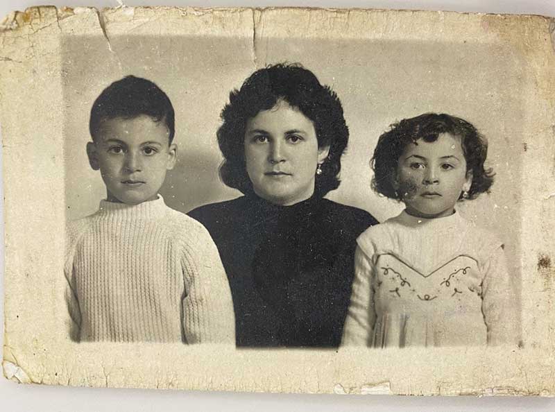 Passport photo of a woman in black and a child on either side of her, wearing white clothing.