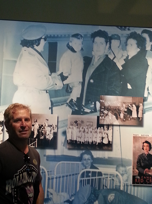 A man stands in front of a display that holds his photo from 51 years ago.