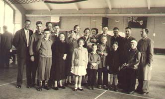 Several men, women and children posing inside large hall area.