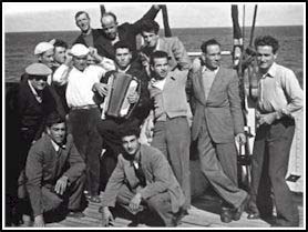 Bruno playing the accordion in the middle of several young men on deck of ship.