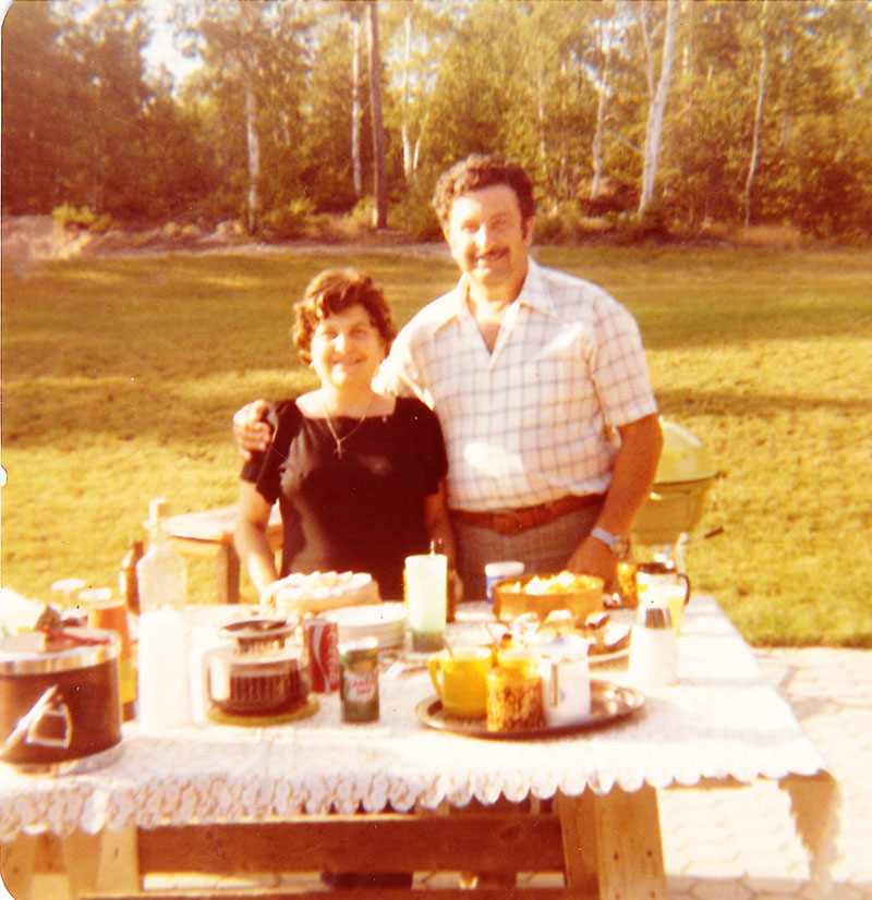 A handsome man and beautiful lady standing behind food table.