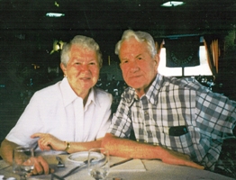Older couple seated at dinner table with wine glasses in front of them.