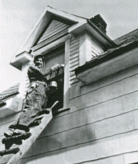 View from below of young Cornelius on ladder painting house.