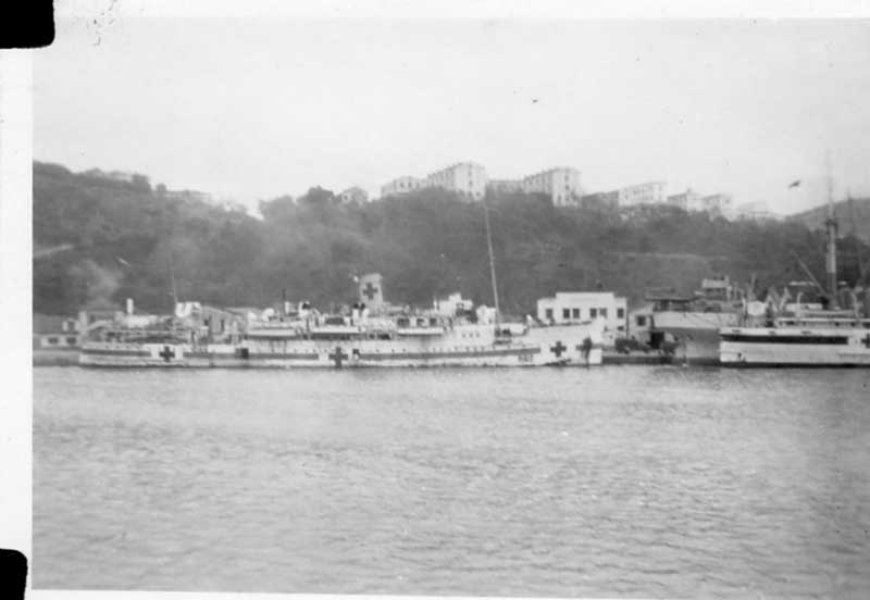 Ships are docked at port, and smoke is billowing from the funnels.