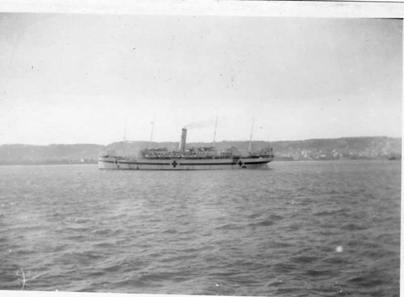 Black and white photo of a sailing ship with a red cross sign and billowing smoke from a funnel.