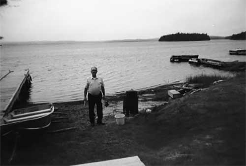 A man stands on a beach next to a small wharf.