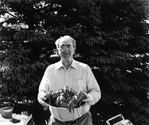 A man stands proudly with an enormous bucket of lobsters.