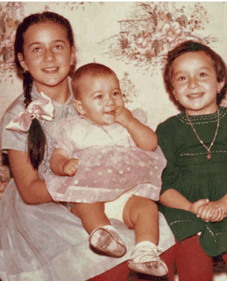 Young girl with long braid holding baby, with little girl in green next to her.