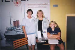 Irene stands with her daughter Fiona, while her granddaughter Sarah sits at a table.