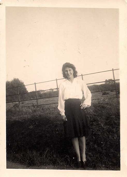 A young woman stands in front of a hedge.