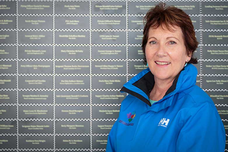 Smiling woman in blue jacket stands in front of a wall with green plaques on it