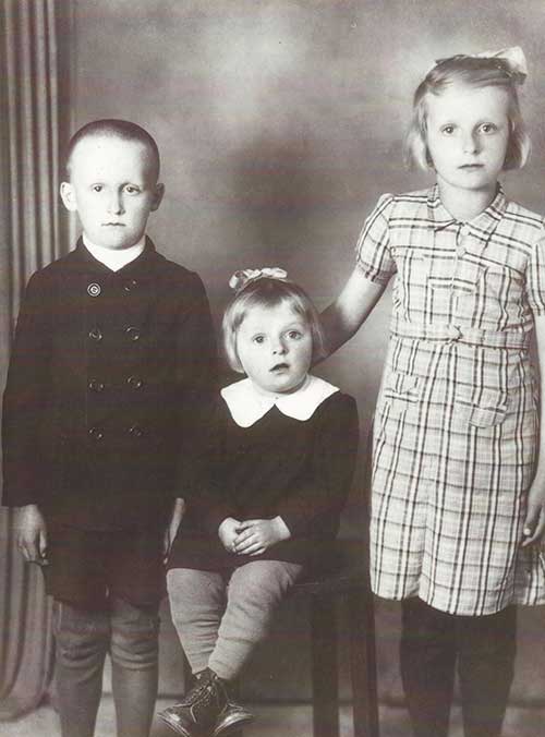 A baby sits on a stool between a young boy and girl.