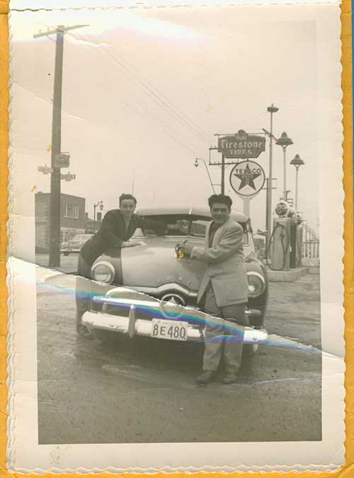 Two well-dressed young men sitting on a car's hood.