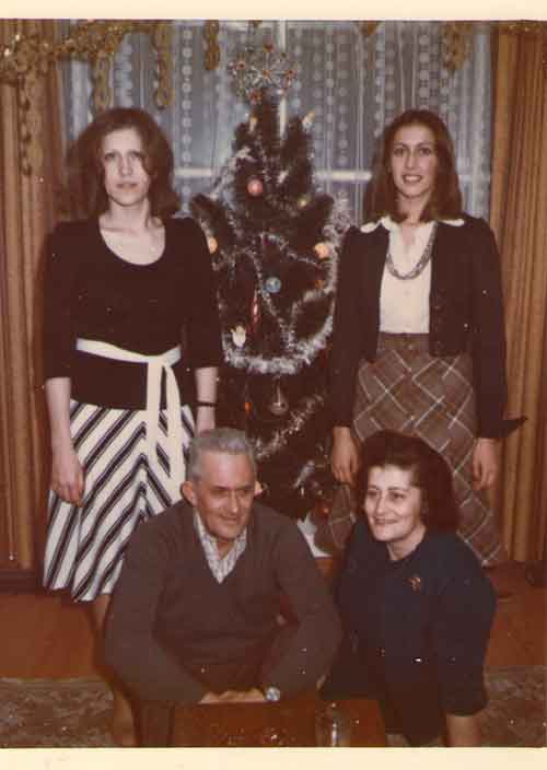 Two young ladies standing on either side of a Christmas tree and a couple seated in front.