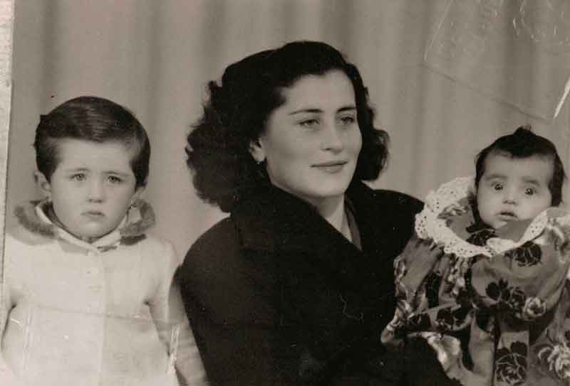 A young woman wearing a winter coat stands with her two children.