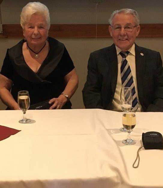 An elderly couple sit at a banquet table and drink white wine.