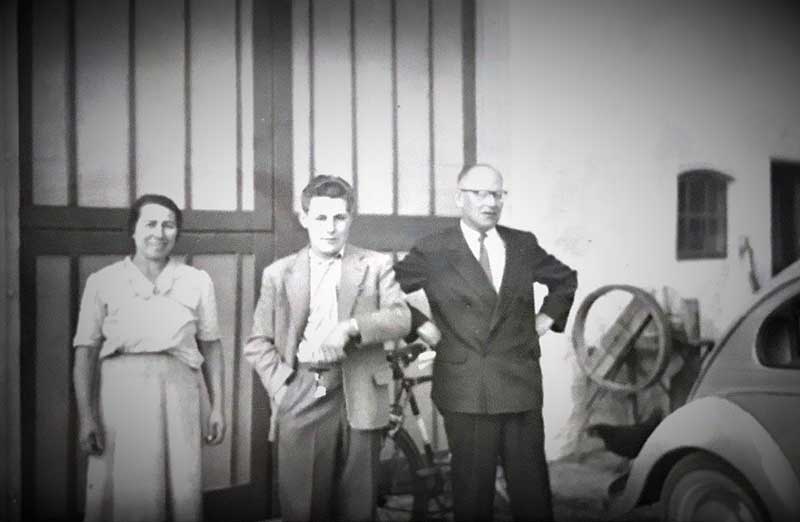 A young man showing a wrist watch stands between an older man and woman.