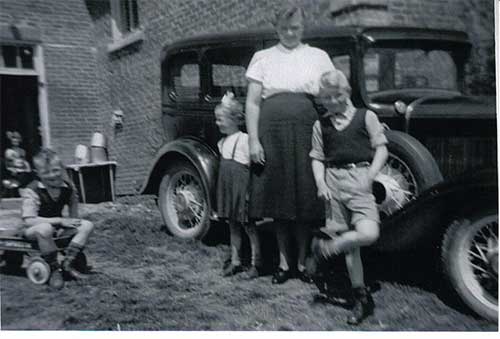 Two children and a woman are standing in front of a car.