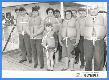 Men, women and children standing on deck of ship wearing life jackets.