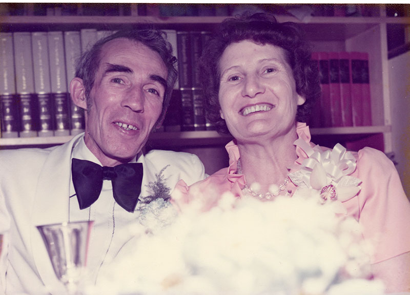 A smiling couple are sitting in front of a book shelf lined with encyclopedias.