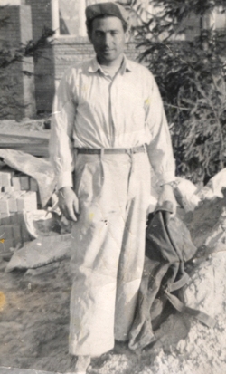 Man in white standing in front of large stones and tree.