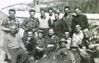 A large group of men are outside, some wearing protective helmets. 
