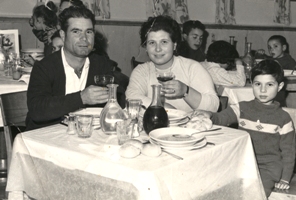 Young man, woman and child sitting at the dinner table loaded with plates and glasses.